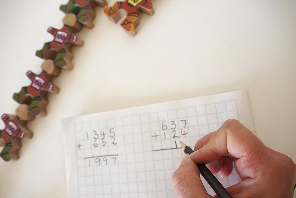 Écrivez ce second chiffre sous le numéro initial sur le papier quadrillé, démontrant la disposition correcte et l'utilisation des signes mathématiques. Laisser une ligne entre les nombres et la réponse permet une transition plus douce vers l'addition dynamique. Demandez à l'étudiant de vous transmettre la quantité correcte de Flockmen pour le second numéro. Au fur et à mesure qu'ils vous les transmettent, comptez-les, en les plaçant dans des colonnes sous l'ensemble initial de Flockmen, en laissant un espace ou en plaçant une règle, entre les deux dispositions (ceci fournit un rappel visuel pour vérifier la somme).