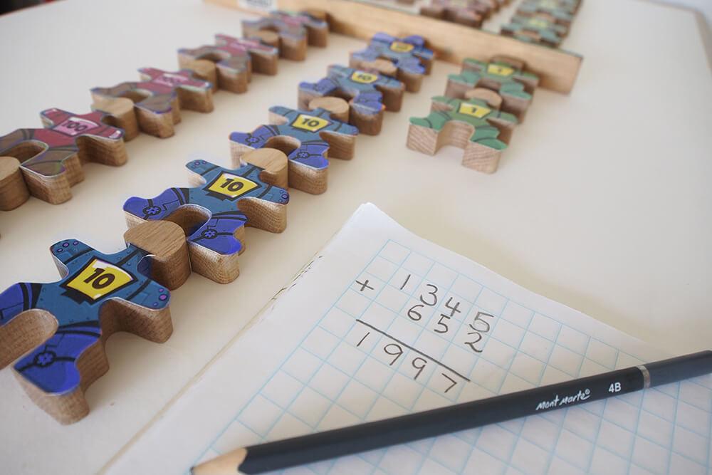 Écrivez ce second chiffre sous le numéro initial sur le papier quadrillé, démontrant la disposition correcte et l'utilisation des signes mathématiques. Laisser une ligne entre les nombres et la réponse permet une transition plus douce vers l'addition dynamique. Demandez à l'étudiant de vous transmettre la quantité correcte de Flockmen pour le second numéro. Au fur et à mesure qu'ils vous les transmettent, comptez-les, en les plaçant dans des colonnes sous l'ensemble initial de Flockmen, en laissant un espace ou en plaçant une règle, entre les deux dispositions (ceci fournit un rappel visuel pour vérifier la somme).